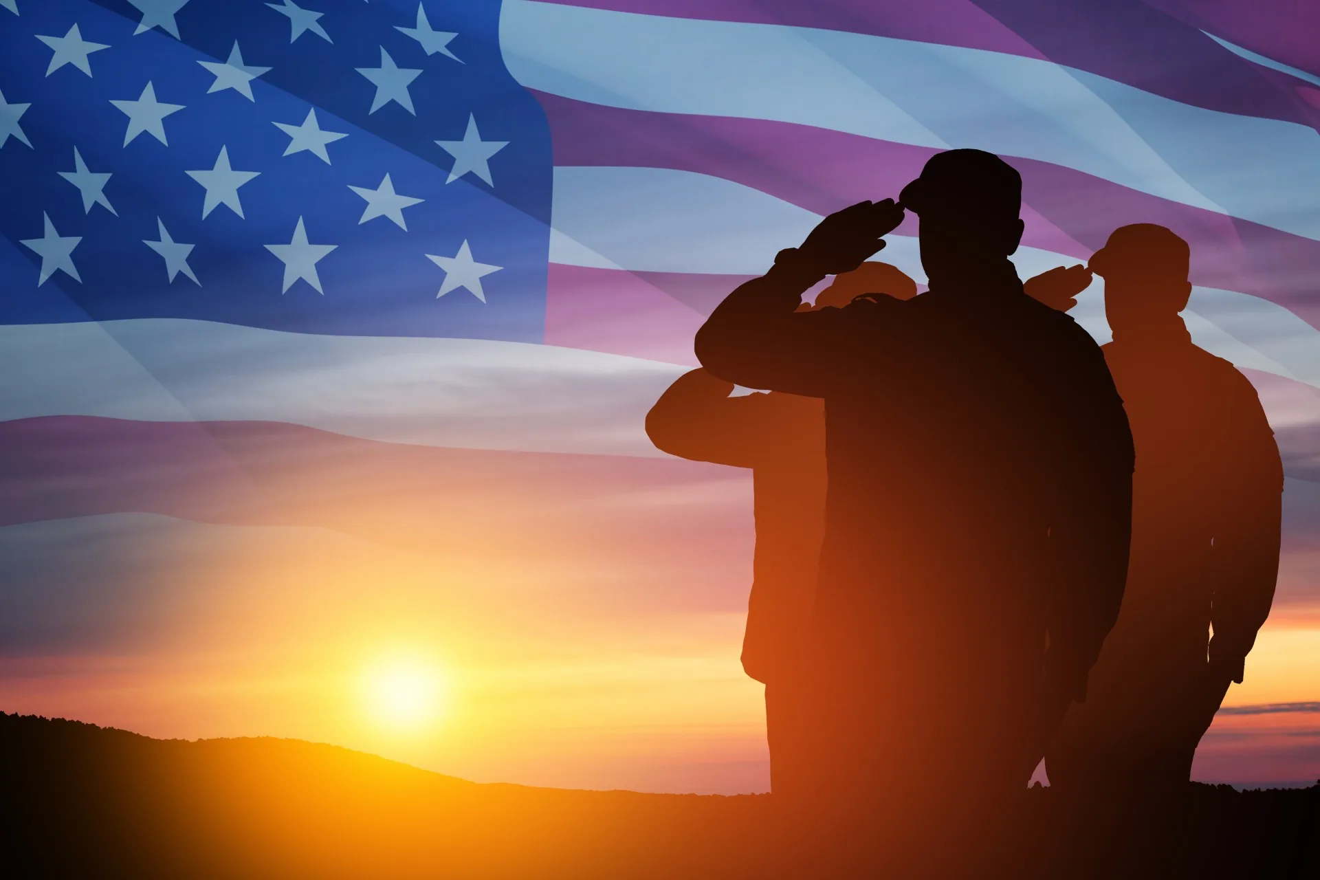 Two veterans saluting at sunset with the American flag behind them